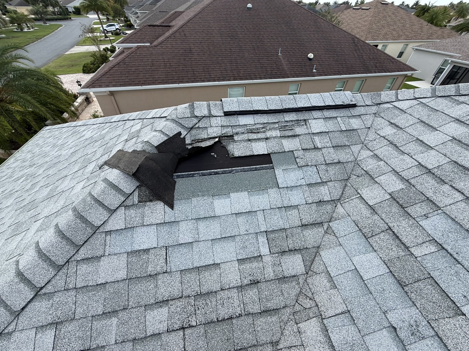 Storm-damaged ridge shingles on a shingle roof